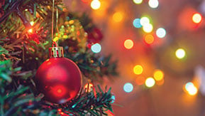 Close-up of a decorated Christmas tree with a red bauble and colorful, blurred lights in the background, creating a festive and warm atmosphere.